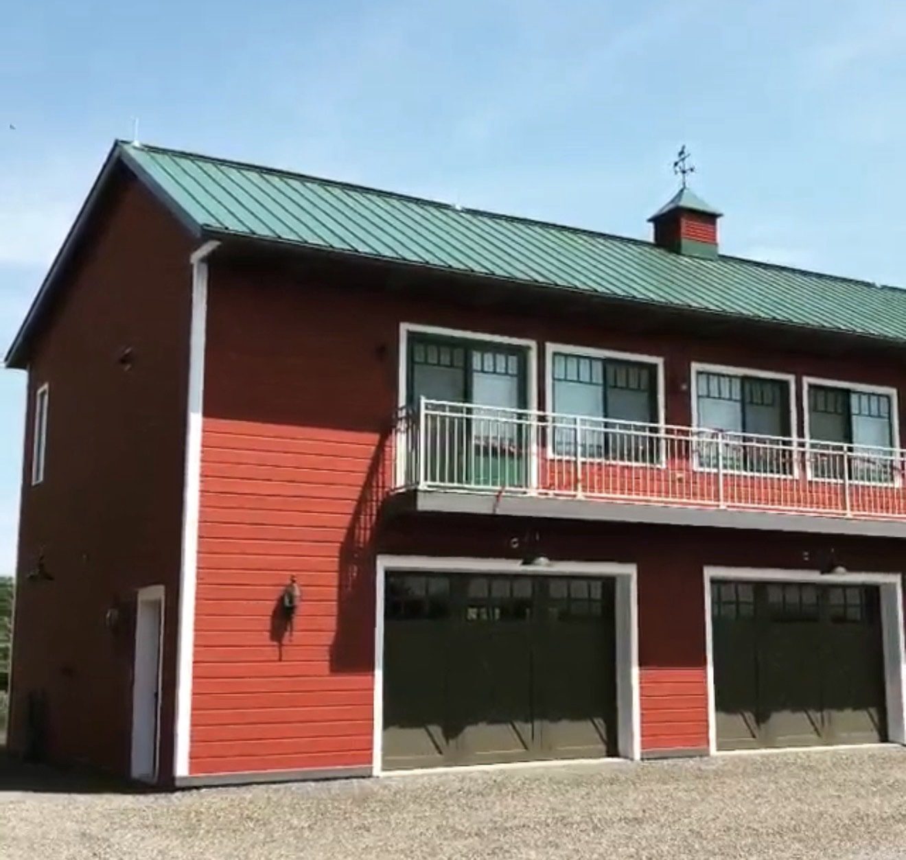 Red carriage house with a green metal roof, balcony, and cupola fitted with a lightning rod and weathervane
